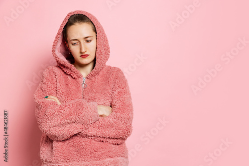 Sad young woman, student with short hair in pearch color hoodie isolated on pink background. Concept of emotions, studying, ad photo