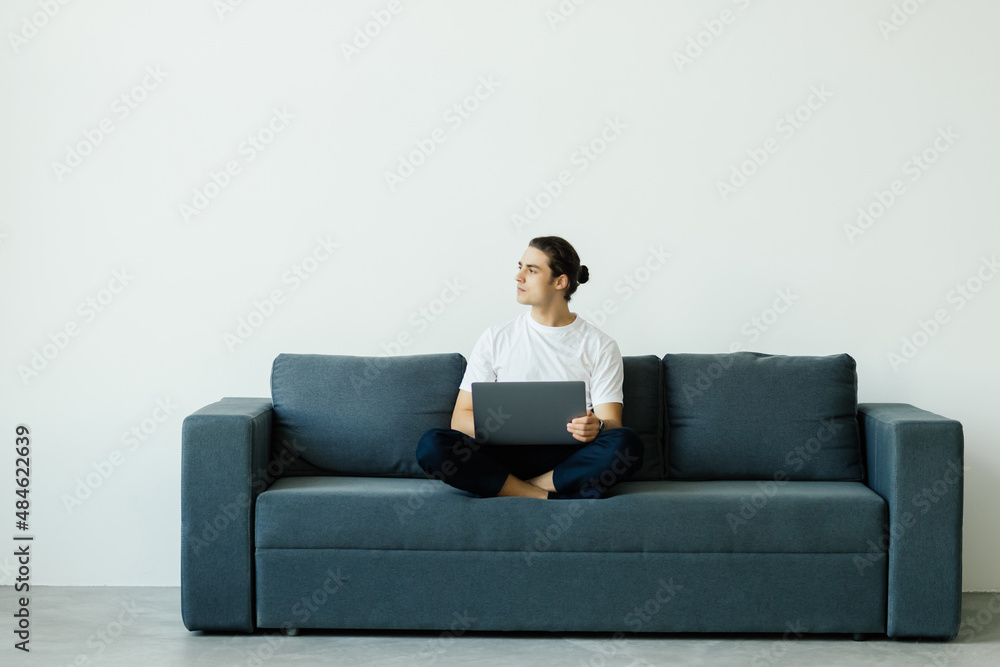 Portrait of young man smiling and using laptop while sitting on sofa at home Portrait of young man smiling and using laptop while sitting on sofa at home