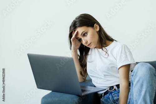 Nervous young woman sitting on sofa, worrying about bad news, received by email on laptop. Stressed businesswoman thinking of crisis challenges, feeling desperate or unsure, stack with hard decision.