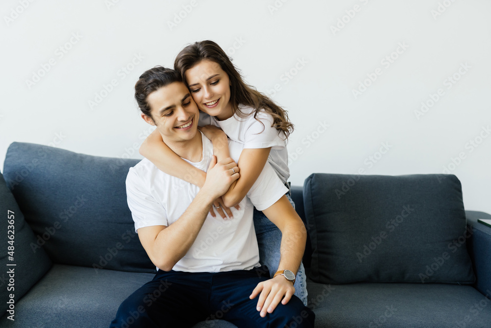 Cheerful couple smiling and hugging while sitting on sofa at home