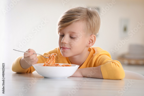 Cute boy eating tasty pasta at table in kitchen