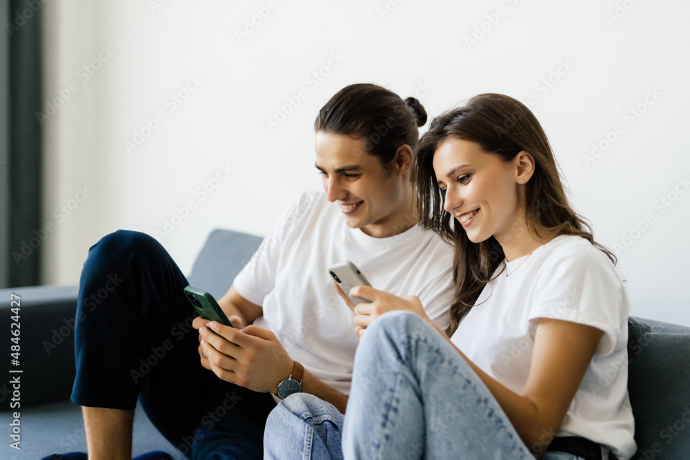 Man and woman sitting on a couch and holding smartphones in their hands. Man and woman sitting on a couch and holding smartphones in their hands.