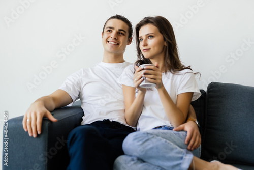 Young couple sitting on a couch at home, watching TV, drinking tea