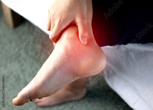 A person holding ankle on Achilles tendon, suffering with pain in red spot area. Sprain ligament or Achilles tendonitis symptoms. Image with red highlights on hurting area, Health care concept photo