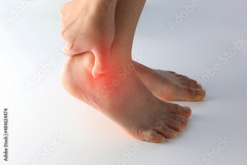 A person holding ankle on Achilles tendon, suffering with pain in red spot area. Sprain ligament or Achilles tendonitis symptoms. Image with red highlights on hurting area, Health care concept photo