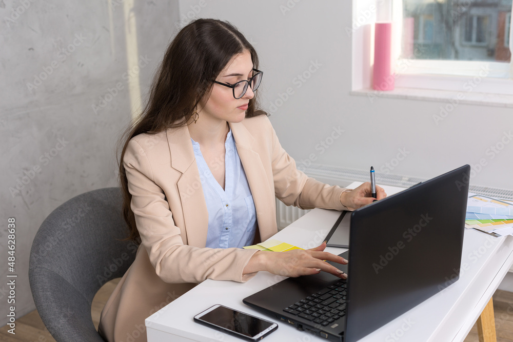 A young designer girl sitting at a table draws on a tablet. Makes business calculations on the computer. A young designer girl sitting at a table draws on a tablet. Makes business calculations on the computer.
