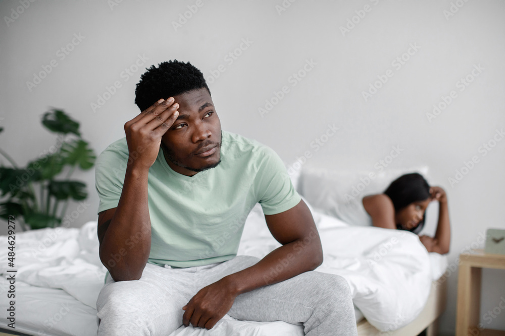 Sad upset millennial african american husband sits on bed and ignores offended wife after quarrel