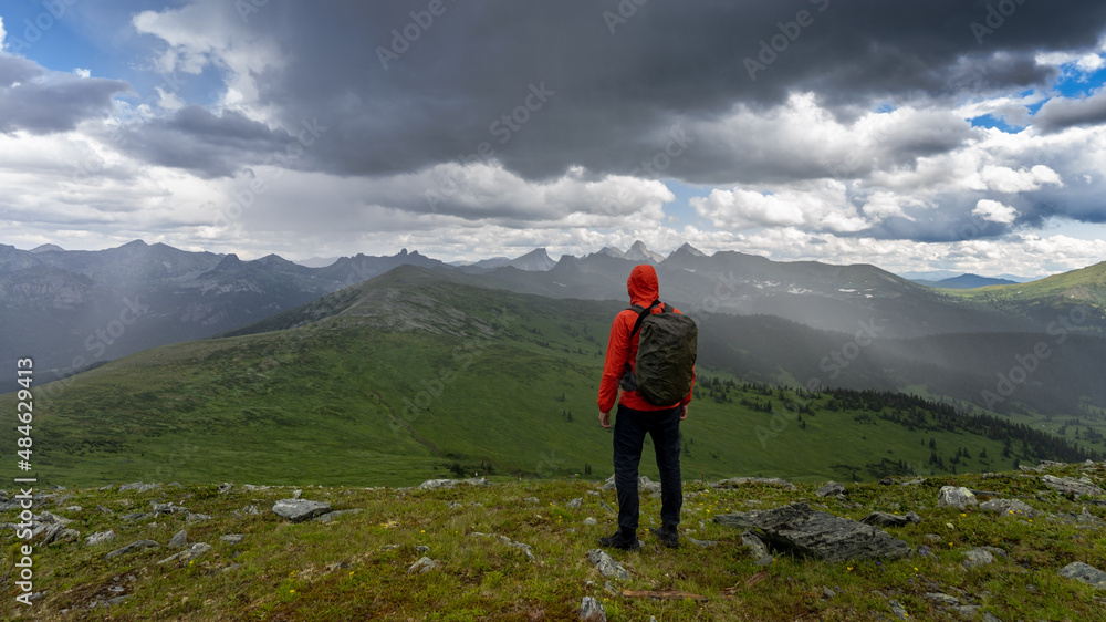 Young man standing on top of a cliff in summer mountains enjoying nature view