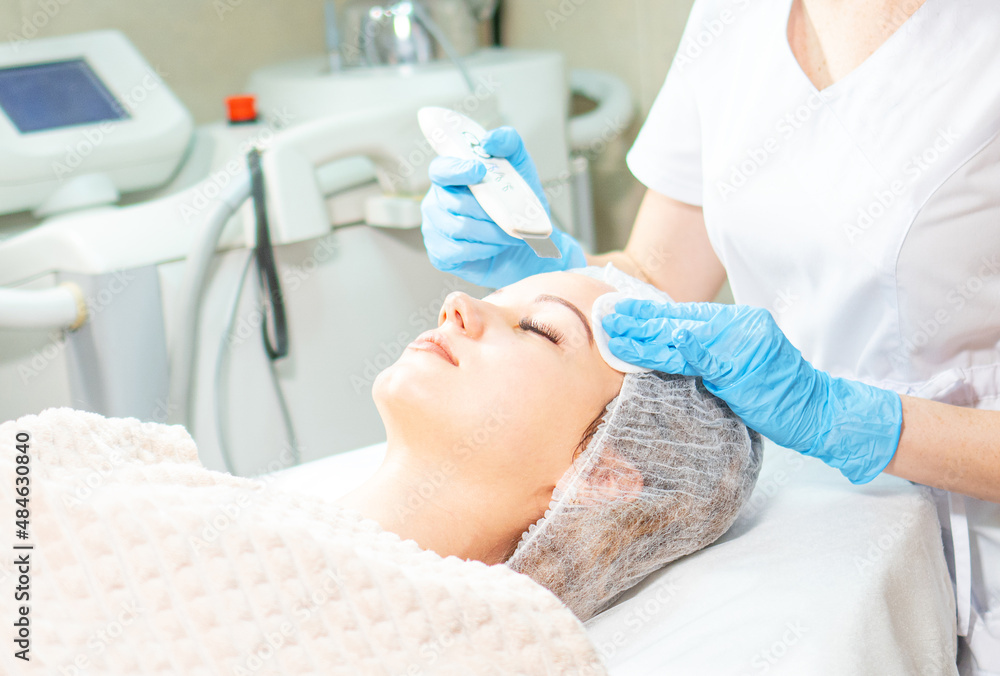 Obraz premium Cosmetology background. Cosmetologist doing ultrasound face peeling for the young woman.