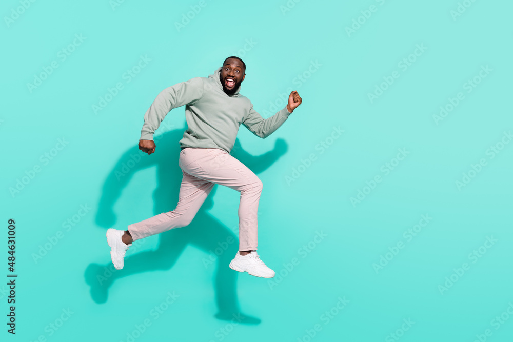 Full length body size view of attractive cheerful active trendy guy jumping running isolated over vivid teal turquoise color background