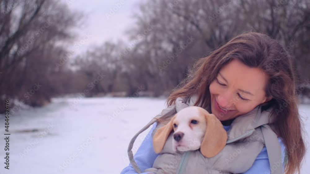 female in jacket hugs with cute beagle puppy on the snowy bank near a frozen river female in jacket hugs with cute beagle puppy on the snowy bank near a frozen river