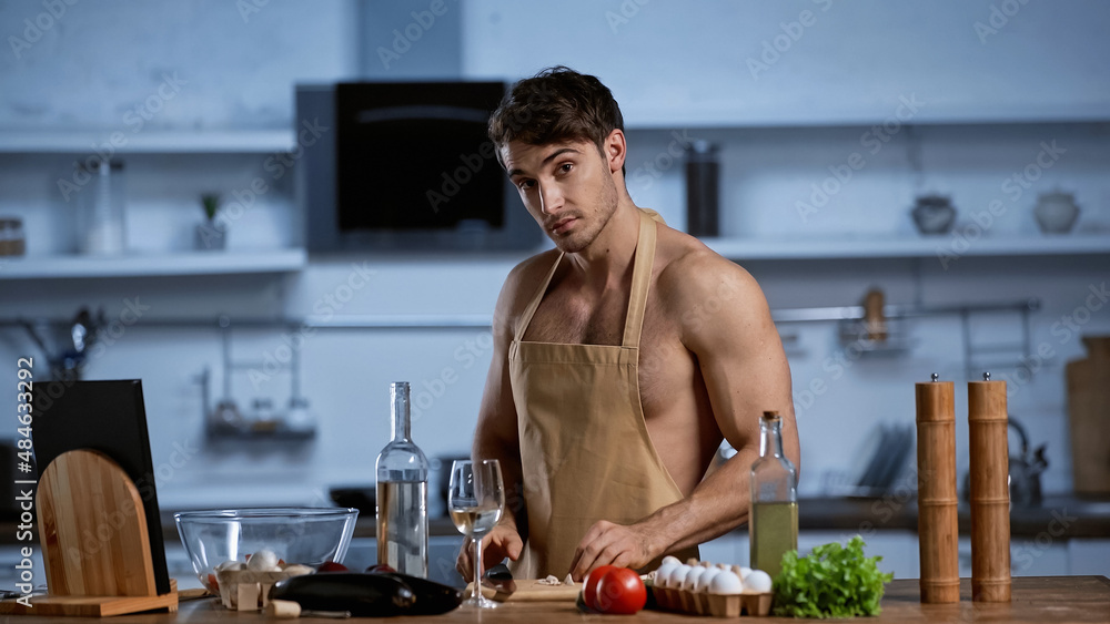 shirtless man in apron cooking in kitchen and looking at camera. shirtless man in apron cooking in kitchen and looking at camera.