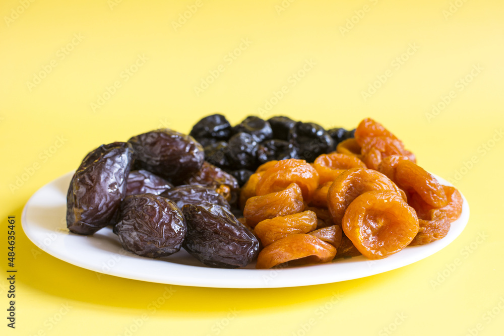 Dried apricots, prunes and dates dried fruits on a light plate close-up. Dried apricots, prunes and dates dried fruits on a light plate close-up.