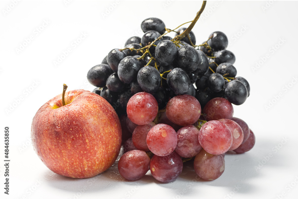 Still life of red and black grapes and a red apple on a light background with water drops. Still life of red and black grapes and a red apple on a light background with water drops.
