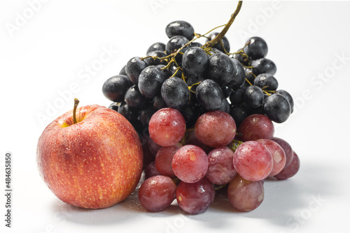 Still life of red and black grapes and a red apple on a light background with water drops.
