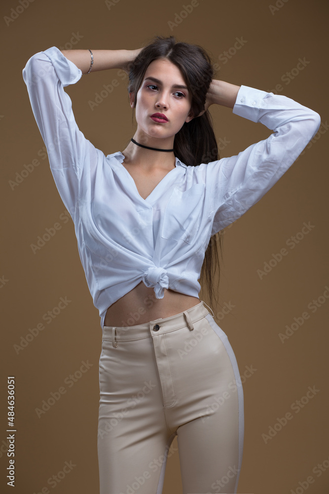 A girl in a white blouse and leather leggings on a beige background A girl in a white blouse and leather leggings on a beige background