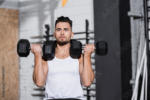 Young sportsman working out with dumbbells in sports center.