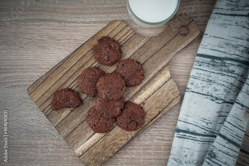 Flat lay cookies on a chopping board and a glass of milk on a table