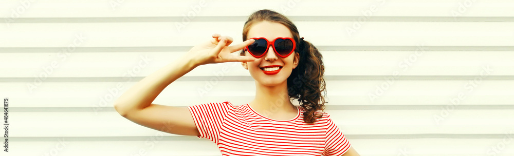 Portrait of happy smiling young woman with cool hairstyle wearing red heart shaped sunglasses, striped t-shirt on white background Portrait of happy smiling young woman with cool hairstyle wearing red heart shaped sunglasses, striped t-shirt on white background