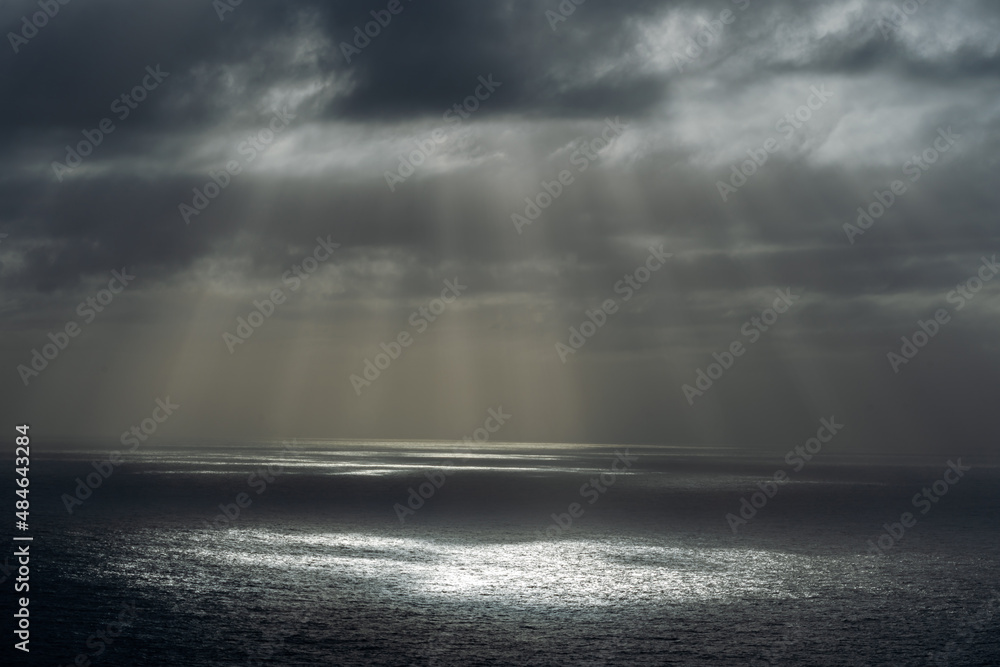 Fototapeta premium Rays of sun through dark clouds at ocean.