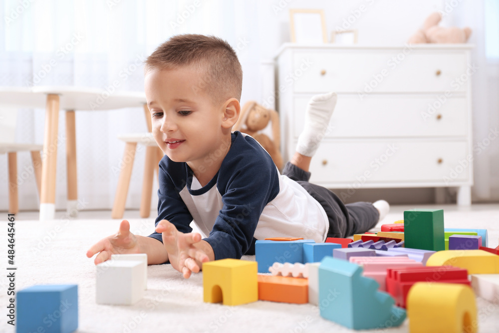 Cute little boy playing with colorful building blocks on floor in room Cute little boy playing with colorful building blocks on floor in room