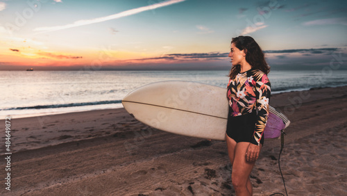 Woman on beach with surfboard and summer neoprene at sunrise