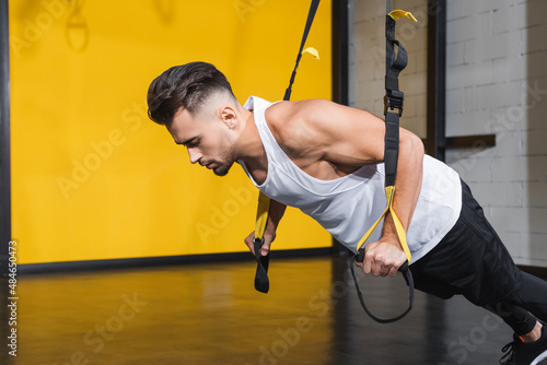 Athletic man working out with suspension straps in gym.