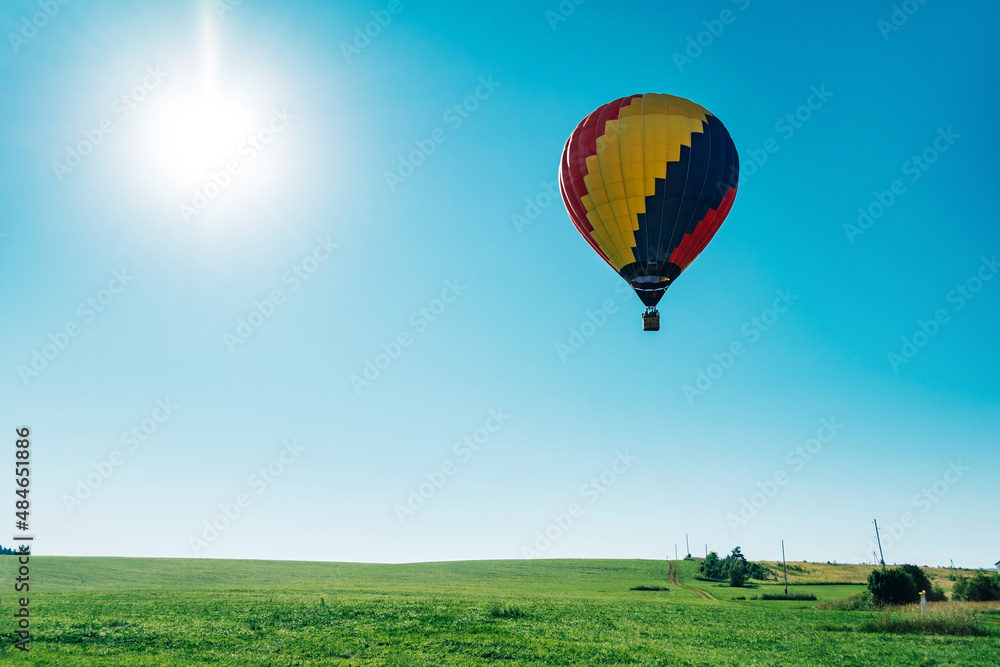 Multicolored hot air balloon on blue sky over village field