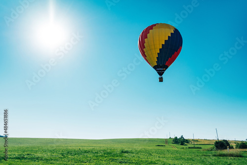 Multicolored hot air balloon on blue sky over village field