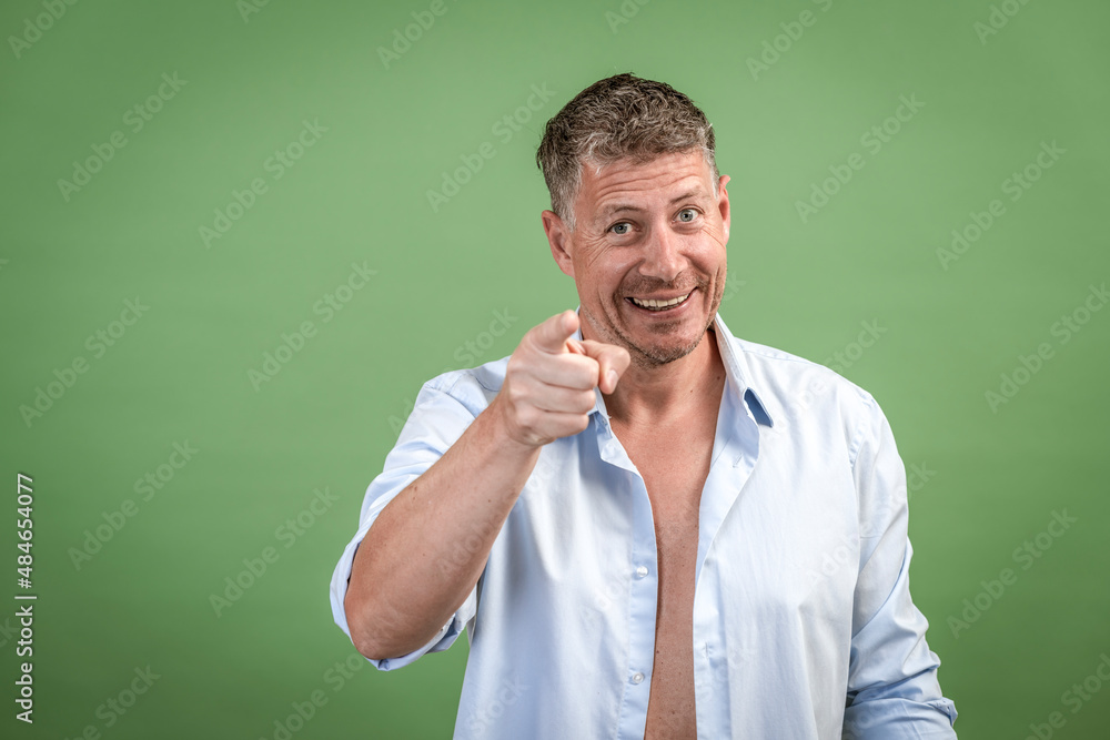 Middle aged man with open blue shirt is standing in front of green wall Middle aged man with open blue shirt is standing in front of green wall