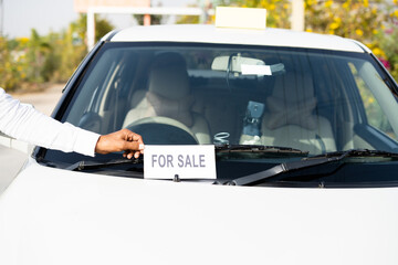 Close up shot of owner placing car for sale sign board in front of car - concept of business loss, personal probleams, financial criss, bankrupt and debt.