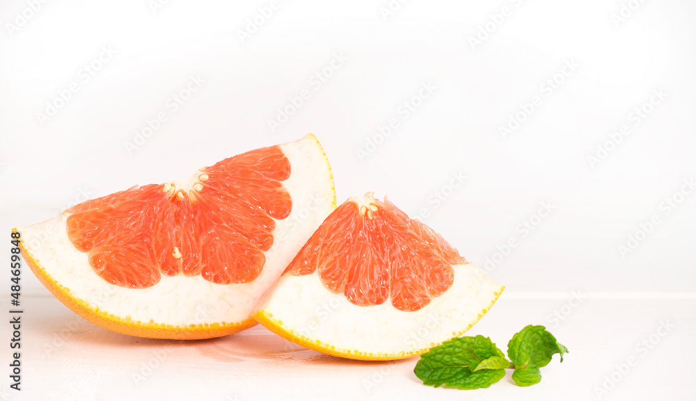 Two slices of grapefruit and a sprig of mint on a light background