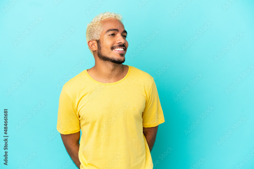 Young Colombian handsome man isolated on blue background looking to the side and smiling Young Colombian handsome man isolated on blue background looking to the side and smiling