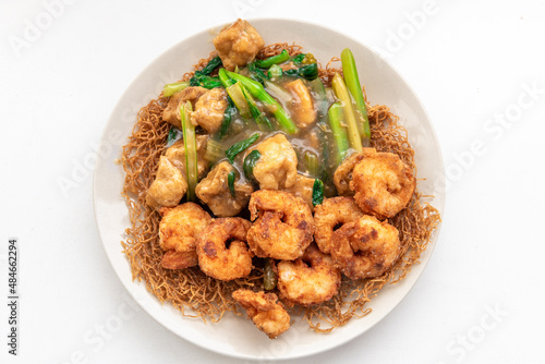 A plate of crispy toasted noodles with fried tofu, king prawns and seasonal green vegetable.