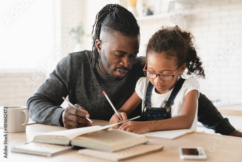 Tutoring homeschooling concept. African father dad childminder helping daughter student with homework, drawing together, e-learning, preparing for school art project at home.