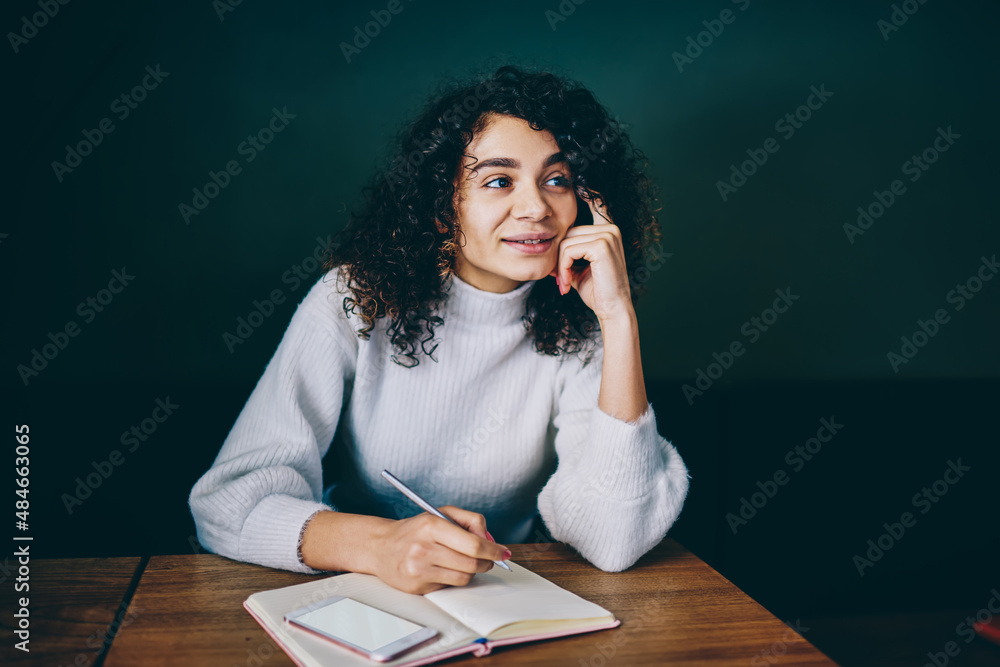 Fototapeta premium Attractive Latin student pondering on education information sitting at desk with textbook and mockup cellular technology with copy space area for web advertising, young woman with blank mobile gadget