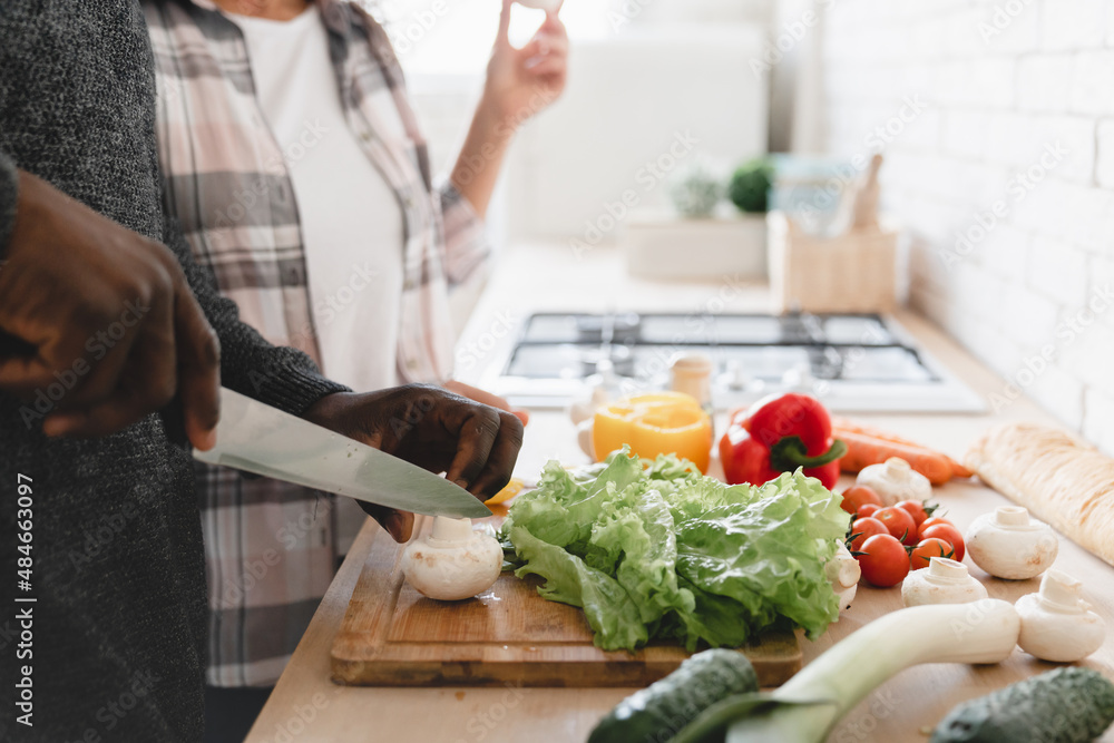 Cropped closeup image of african-american couple spouses cooking preparing vegetarian vegan food meal together at home kitchen, cutting vegetables for salad. Love and relationship concept