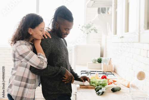 Happy mature middle-aged african-american couple spouses cooking preparing vegetarian vegan food meal together at home kitchen, cutting vegetables for salad. Love and relationship concept