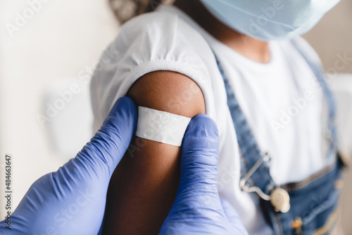 Covid 19 measles, ebola vaccinated. Doctor pediatrician injecting making vaccine to little african girl in medical clinic. Nurse applying medical patch after injection
