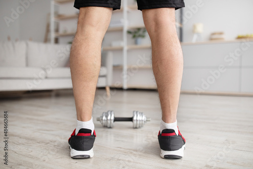 Home workout. Mature man ready fot exercising with dumbbells, working out in living room interior, back view, crop