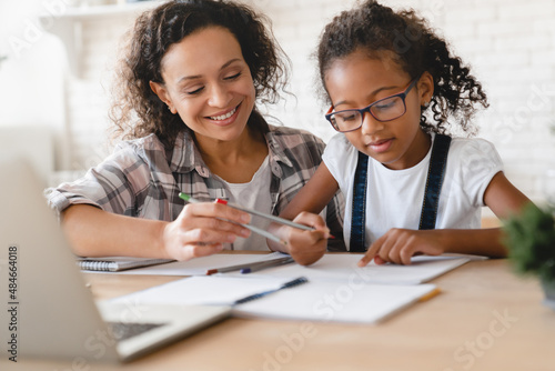 African-american mom mother tutor nanny childminder drawing together helping assisting with homework school project to a preteen daughter. Homeschool concept. E-learning on laptop photo