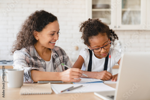 Tutoring homeschooling concept. African mother mom nanny childminder helping daughter with homework, drawing together, e-learning, preparing for school art project at home. © InsideCreativeHouse
