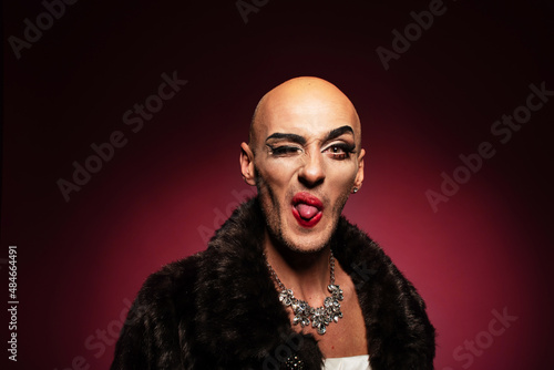 Portrait of gender fluid middle-aged transgender gay man with shaved head winking, showing tongue and making funny face photo