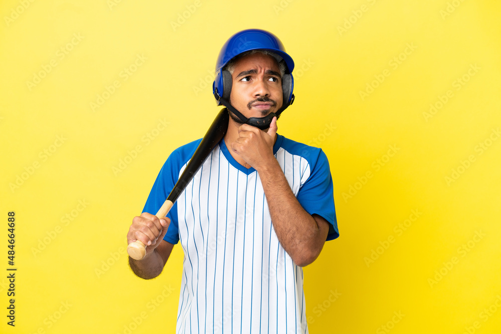 Young Colombian latin man playing baseball isolated on yellow background having doubts