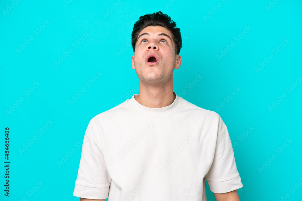 Young handsome caucasian man isolated on blue bakcground looking up and with surprised expression Young handsome caucasian man isolated on blue bakcground looking up and with surprised expression