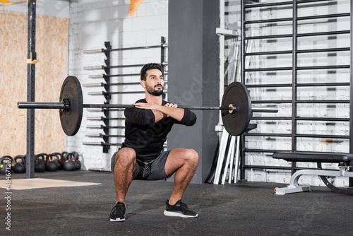 Arabian sportsman lifting barbell in gym.