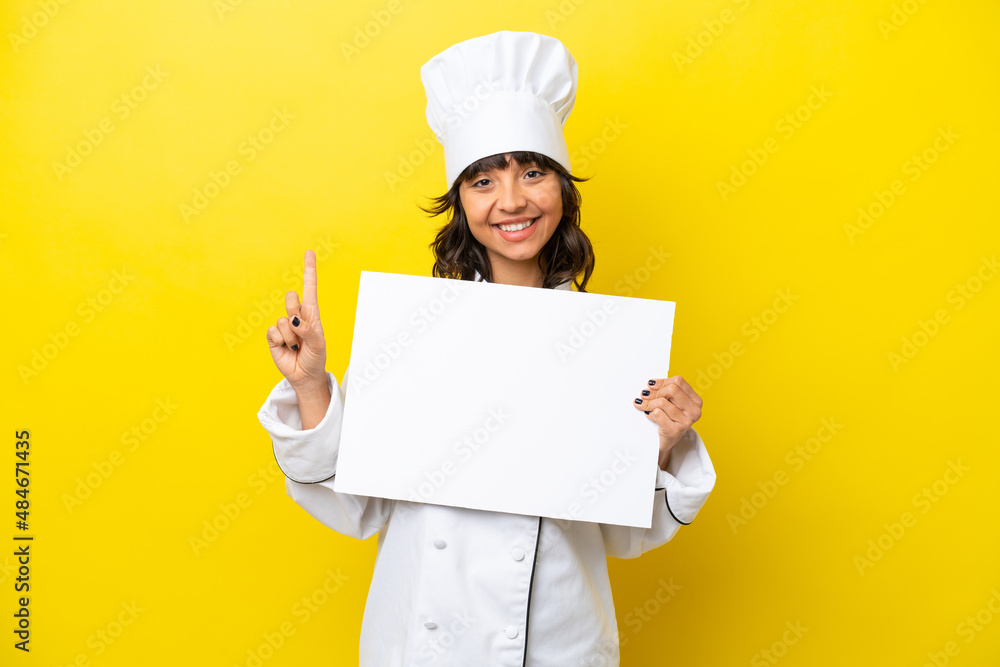 Young chef latin woman isolated on yellow background holding an empty placard and pointing up Young chef latin woman isolated on yellow background holding an empty placard and pointing up