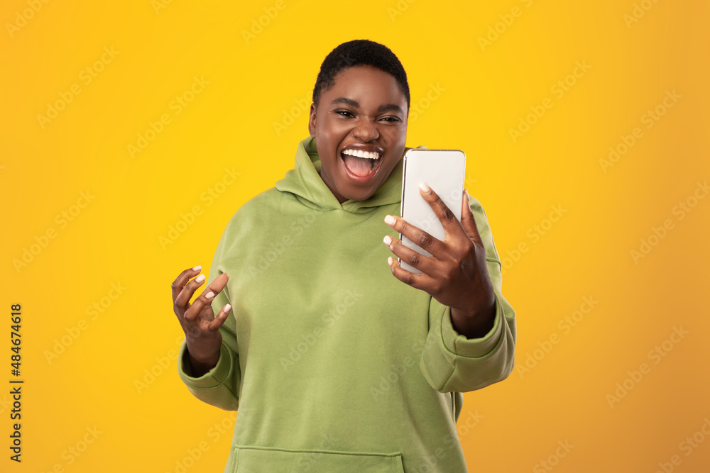 African American Lady Holding Smartphone Shouting Emotionally Over Yellow Background African American Lady Holding Smartphone Shouting Emotionally Over Yellow Background