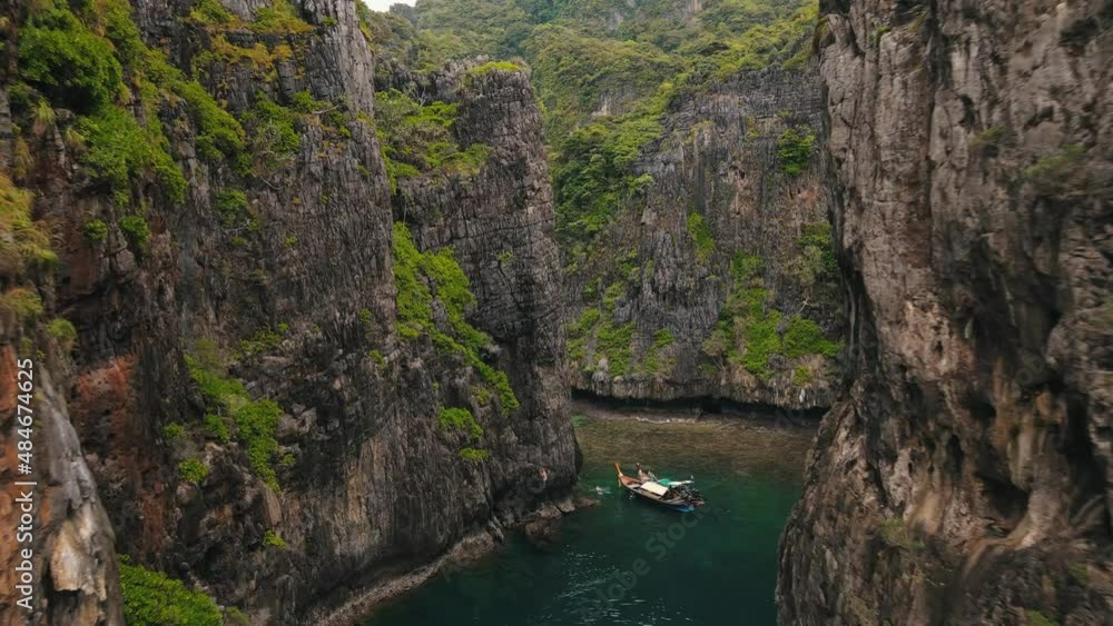 Wang Long Bay hidden behind the enormously steep rock walls which are partly covered with green vegetation while a boat sails across the clear bay. Drone dolly shot Wang Long Bay hidden behind the enormously steep rock walls which are partly covered with green vegetation while a boat sails across the clear bay. Drone dolly shot
