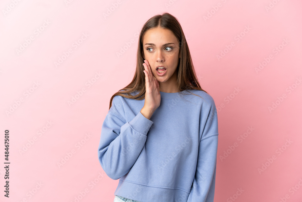 Young woman over isolated pink background whispering something with surprise gesture while looking to the side Young woman over isolated pink background whispering something with surprise gesture while looking to the side